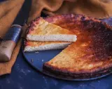 Un fiadone corse, un gâteau au fromage et au citron, est servi avec une tranche coupée, à côté d'un couteau sur un tissu ocre.
