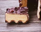 Ein Stück Baumkuchen mit Schokoladenglasur und weißen Zuckerguss-Wirbeln, perfekt für ein Baumkuchen Rezept.