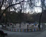 Parque de la Quinta de la Fuente del Berro con niños jugando en columpios y toboganes, rodeado de árboles y una valla colorida.