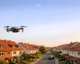 Eine Drohne fliegt über ein ruhiges Wohngebiet. Sie schwebt in 120 m Höhe über den roten Dächern und gepflegten Gärten.