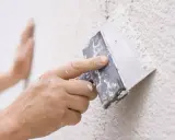Mano aplicando masa con espátula para reparar gotele en pared.