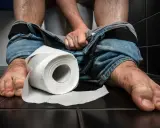 En person sitter på en toalett med neddragna jeans. En rulle toalettpapper ligger bredvid. Tänk på vaccin mot turistdiarré för en tryggare resa.
