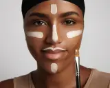 Mujer con líneas de maquillaje para **contouring cara**. Se ve un pincel en su mano.