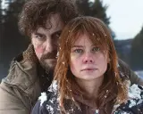 Två personer i snöig skog, en kvinna med rött hår och en man med mörkt lockigt hår. Scen från en svensk deckare serie.