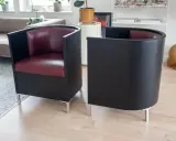 Två svarta fåtöljer med vinröda sitsar, designade av Mats Theselius, står på ett ljust trägolv.
