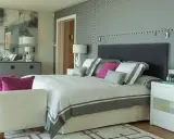 Ideas para diseñar tu habitacion: cama moderna con detalles grises y rosas, mesitas blancas, sofá y espejo decorativo.