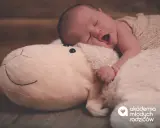 Słodkie niemowlę śpi z otwartą buzią, wtulone w pluszową owieczkę.