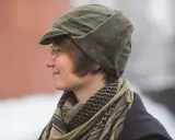 Osoba w okularach nosi zieloną czapkę polową z futrzanymi nausznikami i szalik w stylu keffiyeh.