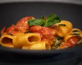 Paccheri alla Vittorio, un piatto di pasta succulenta con pomodoro fresco e basilico, servito in una ciotola scura.