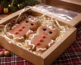 Deux adorables biscuits de Noël en pain d'épice, décorés de glaçage blanc et de bonbons rouges, sont présentés dans une boîte en carton.