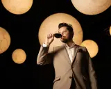 Un homme en costume déguste un verre de vin rouge, entouré de lumières rondes évoquant des planètes. Une dégustation qui rappelle la philosophie du vin biodynamique.