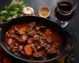 Un plat de vin avec bœuf bourguignon mijoté, garni de carottes et champignons, accompagné d'un verre de vin rouge.