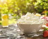 Crème chantilly aérienne et généreuse dans un bol, prête pour un dessert d'été. Une boisson fraîche et des fraises complètent ce tableau gourmand.