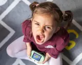 Niña con expresión de enfado y consola de videojuegos, un ejemplo de comportamiento disruptivo significado.
