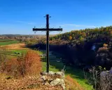 Czarny krzyż na skale góruje nad jesienną doliną Grzybowską. W oddali widać pola i lasy w barwach złota i czerwieni.