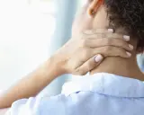 Frau mit Hand am Nacken, die Schmerzen andeutet. Wann zum Arzt bei Nackenschmerzen?