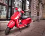 Czerwony skuter, idealny do miasta, kategoria AM. Stylowy pojazd na chodniku przed budynkiem.
