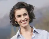 Mujer sonríe con pelo corto rizado y pendientes dorados.