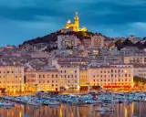 Porto di Marsiglia illuminato al tramonto, con la Basilica di Notre-Dame de la Garde in cima alla collina. Perfetto per le tue marsiglia escursioni fai da te.