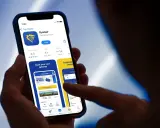 Dłoń trzyma smartfon z otwartą aplikacją Ryanair, widoczna jest strona główna z opcją rezerwacji lotów.