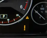 Na desce rozdzielczej świeci żółty trójkąt z wykrzyknikiem, sygnalizując problem. Obok wskaźnik temperatury silnika.