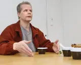 Kaj Linna gestikulerar vid ett bord med tre små mörka koppar framför sig.