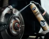 Ręka w czarnej rękawiczce rozpyla środek na zużyte tarcze hamulcowe. Preparat K2 Brake Cleaner skutecznie czyści hamulce.