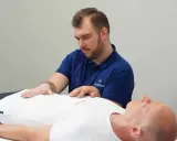 Terapeuta wykonuje zabieg z zakresu osteopatii wisceralnej, delikatnie dotykając brzucha pacjenta.