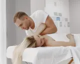 Fizjoterapeuta wykonuje neuromobilizację nerwu promieniowego u pacjentki leżącej na kozetce.