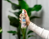 Dłoń trzyma butelkę K2 SKIRON ODOR REMOVAL, która rozpyla mgiełkę, by zlikwidować nieprzyjemny zapach w pokoju po nocy.