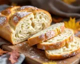 Pain viennois moelleux, saupoudré de sucre glace, coupé en tranches sur une planche en bois, avec des feuilles d'automne en arrière-plan.