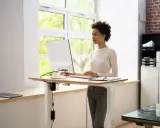 Une femme travaille sur un ordinateur à un bureau réglable en hauteur. La position debout prolongée présente des risques pour la santé, il est donc important de varier les postures.