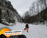 Zimowe jednodniowe wycieczki w góry z Krakowa. Kobieta z psem spaceruje po ośnieżonym szlaku wśród skał i drzew.