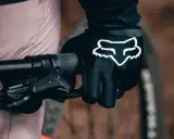 Dłoń w czarnej rękawiczce Fox z białym logo, gotowa do jazdy. Idealne rękawiczki na rower dla każdego miłośnika dwóch kółek.
