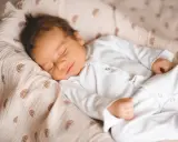 Un neonato dorme sereno, avvolto in una copertina con arcobaleni. Un dolce sogno per questi bambini piccoli.