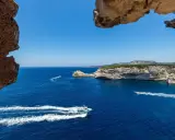 Blick durch Felsformationen auf das tiefblaue Meer bei Bonifacio, Korsika. Boote gleiten über die Wellen.