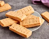 Goldbraune Shortbread-Kekse, perfekt für ein einfaches Shortbread Rezept. Sie liegen auf einem Teller und daneben ein lila Tuch.
