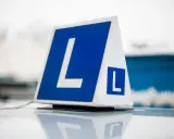 Tablica "L" na dachu samochodu, symbolizująca naukę jazdy. Zastanawiasz się nad **PKK cena**? To pierwszy krok do zdobycia prawa jazdy.