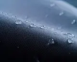 Krople wody na ciemnoszarej tkaninie. Czy nylon oddycha? Woda perli się na powierzchni, nie wsiąkając.