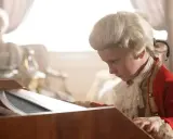Chłopiec w peruce i stroju z epoki gra na klawesynie, przypominając młodego Wolfganga Amadeusza Mozarta.