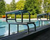 Zwei Sprungbretter am Beckenrand eines Freibades mit Bäumen im Hintergrund.