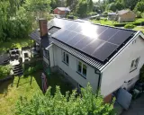 Ett hus med solpaneler på taket, redo att fånga solens energi. En grönskande trädgård och en altan inbjuder till avkoppling.