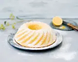 En saftig sockerkaka citron, pudrad med florsocker, serveras på ett fat. En halv citron och en kniv syns i bakgrunden.