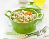 Un tazón verde vibrante lleno de arroz con verduras para bebé, con zanahorias y guisantes.
