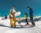 Grupa narciarzy i snowboardzistów na ośnieżonym stoku z widokiem na góry.