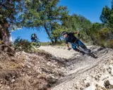 Due ciclisti affrontano un sentiero sterrato in discesa, immersi nella natura. La **tonezza del Cimone** si percepisce nell'aria fresca e nel paesaggio montano.