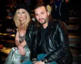 Steve Angello fru, Isabella, med sin blonda frisyr och hatt, sitter bredvid honom. Båda bär svarta läderjackor.
