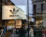 Witryna sklepu z logo adidas, marki pochodzącej z Niemiec. Wieszaki z ubraniami, w tym kurtki i bluzy z charakterystycznymi trzema paskami.