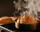 Pain moulé tout juste sorti du four, dégageant une vapeur réconfortante. Une autre miche est prête sur une planche.