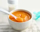 Un tazón con puré de calabaza bebé, una cuchara rosa y un biberón.